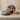 A round, blue and gold gift box with an orange ribbon sits open on a table, filled with assorted candies. Three small, wrapped presents are arranged around it on a neutral background.