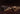 Two types of chocolate bars with cream-colored and dark layers are broken into pieces and placed on a dark brown surface, showing smooth textures and layered interiors. - AI generated text