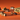 Assorted gourmet chocolates and confections, including layered squares, nut-filled pieces, and chocolate-coated candies, are arranged on an orange surface with a warm light. - AI generated text
