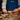 A person in a blue Venchi apron arranges assorted pieces of chocolate on small plates and wooden boards on a rustic table, surrounded by cocoa beans and hazelnuts. - AI generated text