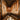 A narrow, luxurious lounge with tufted brown leather seating along both sides, textured gold walls, and small round tables. The space is warmly lit, creating an intimate and elegant atmosphere. - AI generated text