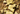 Broken pieces of pistachio chocolate bars resting on a bed of whole, unshelled pistachios. The chocolate is light brown and studded with pistachio pieces, and the bar segments show engraved numbers and letters. - AI generated text