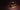 A wooden box with an open lid displays rows of cigars, each in its own slot. Two cigars rest outside the box on a dark surface, set against a moody brown background. - AI generated text